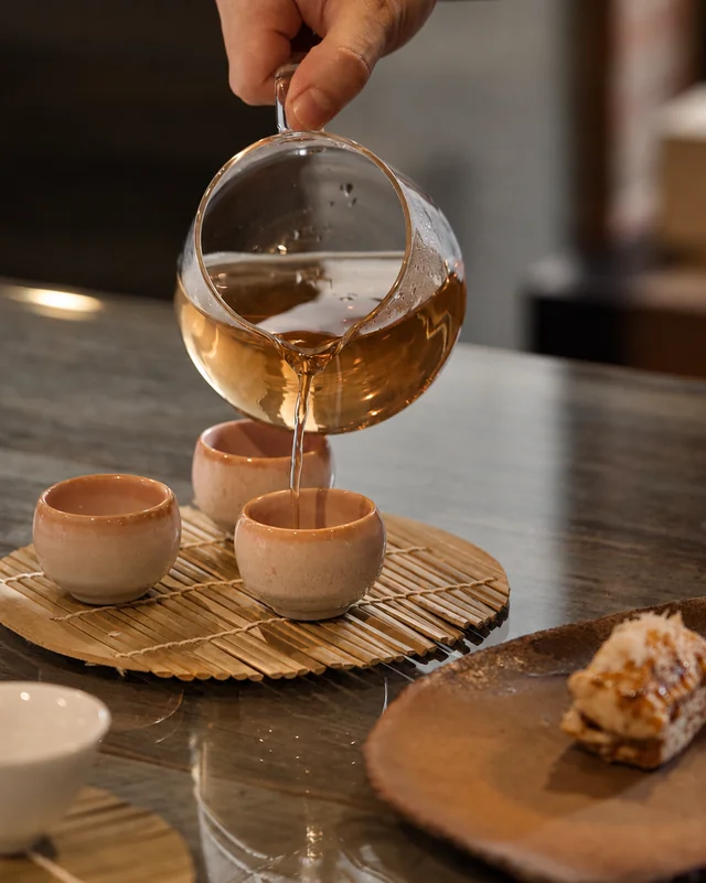 Tea poured from a glass pitcher into warm clay cups.